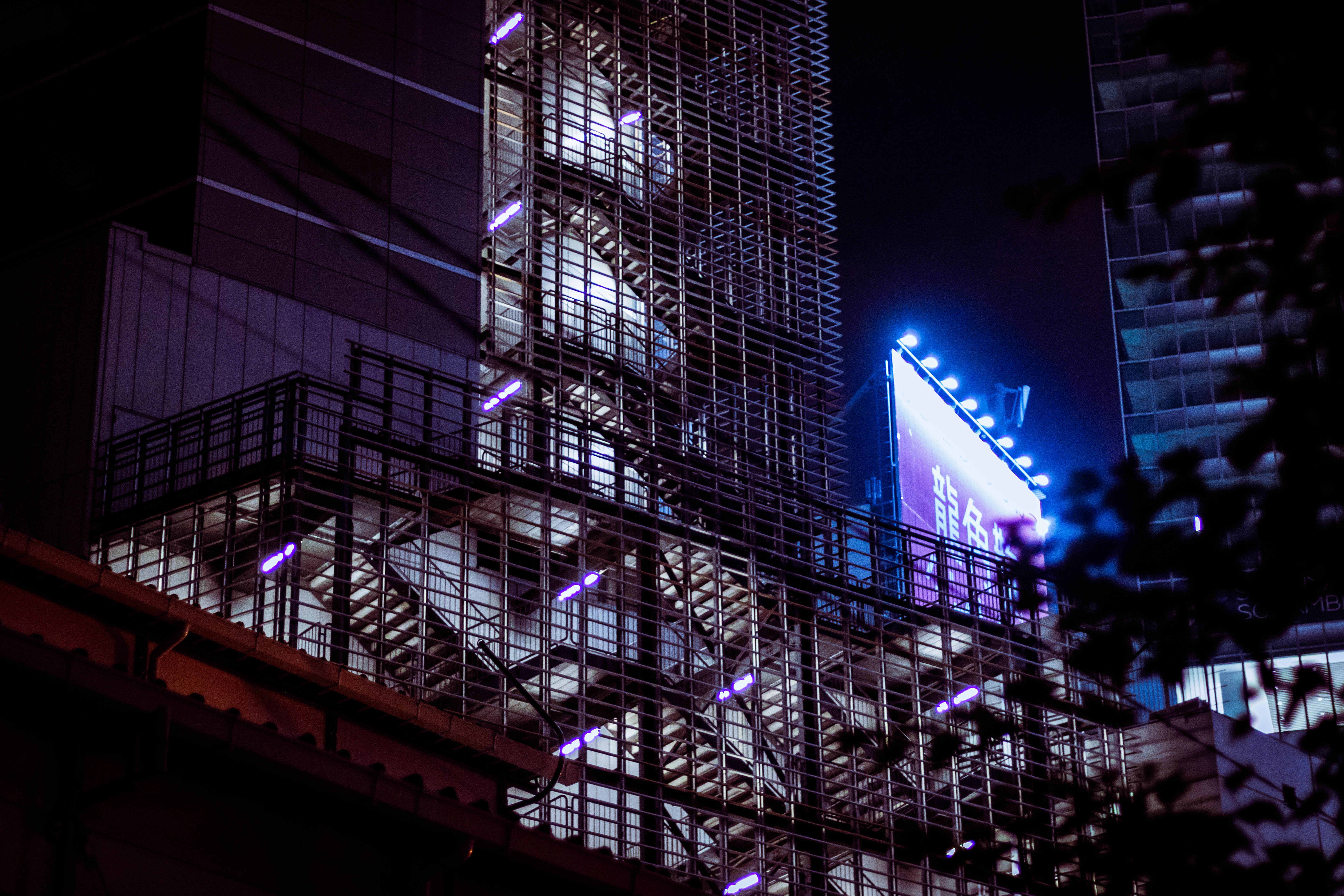 Outdoor stairway protected by an array of horizontal bars next to which a billboard with blue lighting shines.